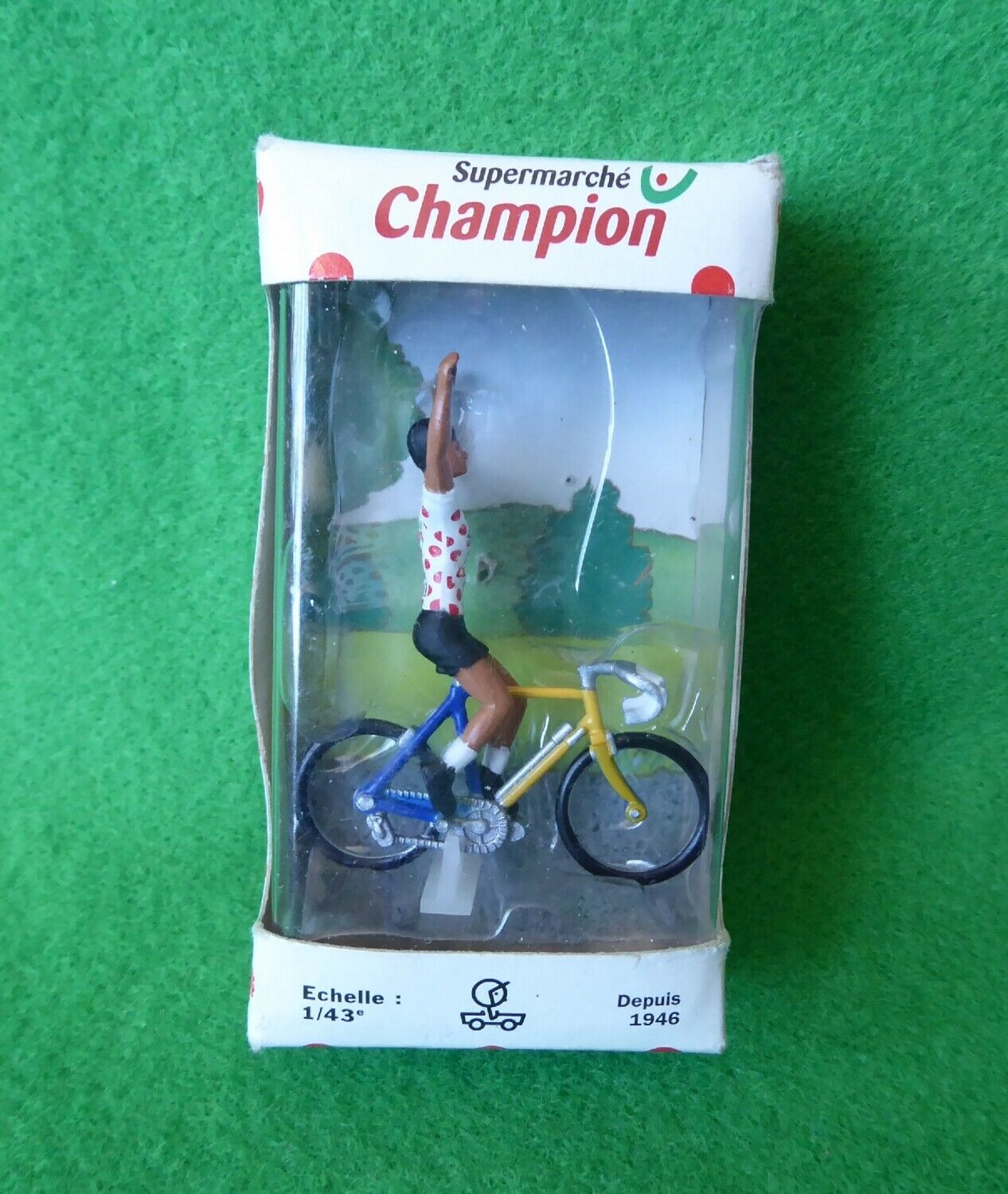 Miniature cyclist raising both arms in its original Champion box