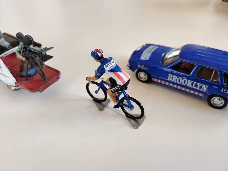 Miniature Brooklyn cyclist between a team car and camera car