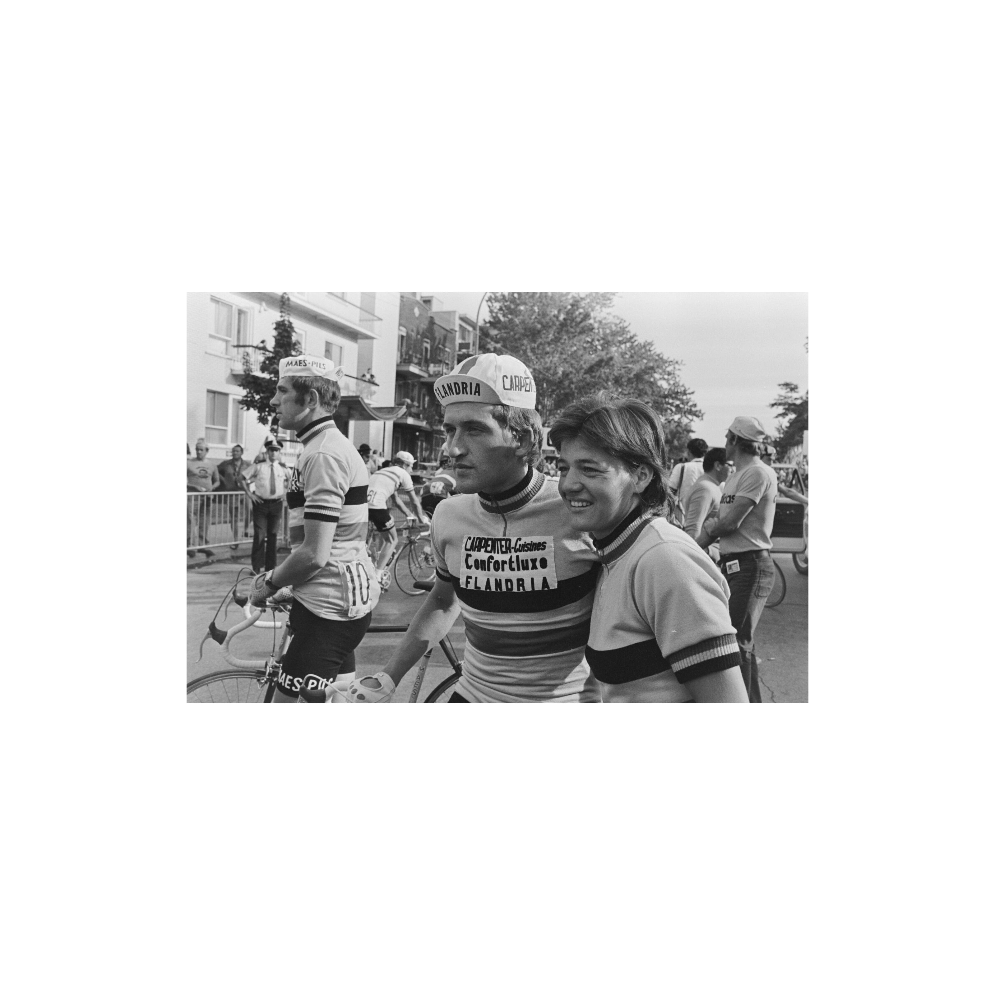 Black-and-white photograph of Freddy Maertens with his bicycle and Mariette Laenen beside him, with other riders and spectators in the background.