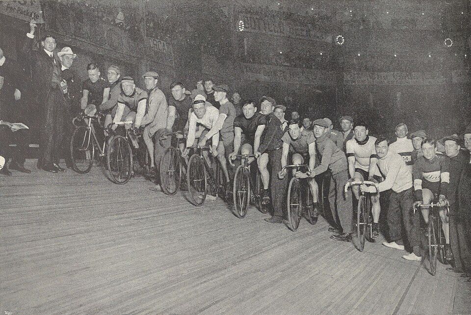A line of six-day riders waiting on an indoor wooden track